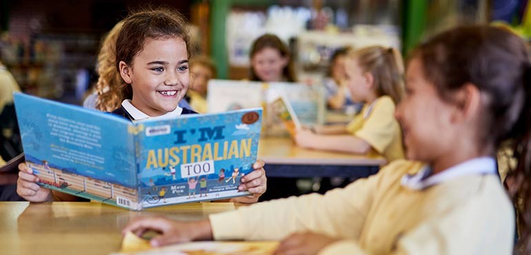 Little girl smiles as she reads the book I'm Australian Too by Mem Fox. 