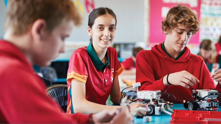 Three high school students sitting at a classroom desk working with robotics.